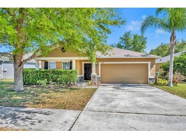 Inviting single-story home featuring a manicured lawn, two-car garage, and a charming, covered entryway at 5910 Windsong Oak Dr, Leesburg, FL 34748