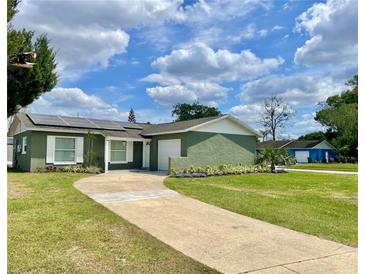 Charming, green single-story home featuring a welcoming front lawn, a driveway, and solar panels on the roof at 714 West Ct, Longwood, FL 32750