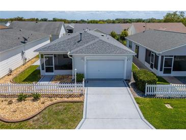 Charming single-story home with a well-manicured lawn, white picket fence, and attached two-car garage at 8233 Se 169Th Palownia Loop, The Villages, FL 32162