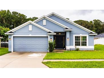 Charming single-story home featuring a well-manicured lawn, two car garage and stylish blue paint at 7732 Sloewood Dr, Leesburg, FL 34748