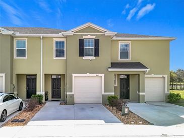 Two-story townhome featuring an attached garage, neutral-tone stucco exterior, and well-manicured landscaping at 965 Lido Dr, Howey In The Hills, FL 34737