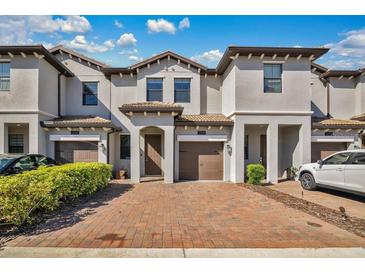 Townhouse exterior with brick paved driveway, brown garage doors, and neutral paint against a blue sky at 1298 Royal St George Blvd, Davenport, FL 33896