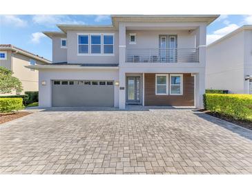 Contemporary two-story home featuring a balcony, gray stucco, a two-car garage, and a brick driveway at 501 Burma St, Kissimmee, FL 34747