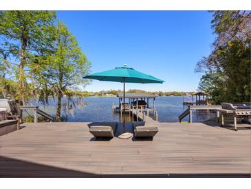 Lounge chairs and outdoor umbrella on deck with lake and dock views at 7841 Georgeann St, Winter Park, FL 32792