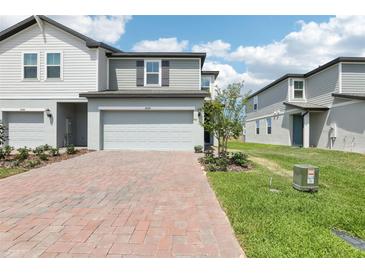 Charming townhome featuring a brick driveway, two-car garage, and neutral-toned siding under a bright, partly cloudy sky at 16450 Bird Of Paradise Ave, Clermont, FL 34714