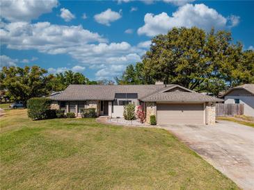 Charming single-story home with a lush green lawn, stone accents, and mature trees under a bright, cloudy sky at 9501 Holbrook Dr, Orlando, FL 32817