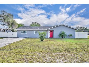 Charming single-story home featuring a red front door, well-manicured lawn, and white fence at 397 Oslo Dr, Deltona, FL 32725