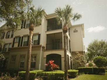 Three-story condo building with a beige facade, black shutters, well-manicured landscaping, and two palm trees at 8276 Maritime Flag St # 201, Windermere, FL 34786