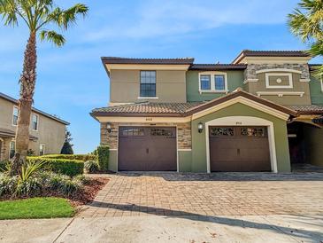 Two-story exterior showcasing a brick driveway, attached garages, and green paint accented by stonework details at 8908 Azalea Sands Ln, Davenport, FL 33896