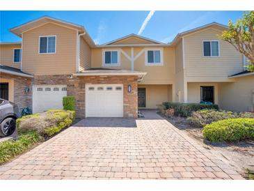 Front exterior view of a tan and yellow townhouse with a brick paved driveway at 10124 Shadow Leaf Ct, Orlando, FL 32825