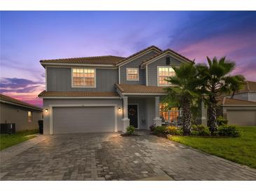 Charming two-story home with a tile roof, lush landscaping, and a paver driveway at dusk at 1158 Oak Bluff Dr, Davenport, FL 33837