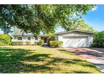 Charming single-story home featuring a manicured lawn, brick accents, attached two-car garage, and mature trees at 2545 Dellwood Dr, Orlando, FL 32806