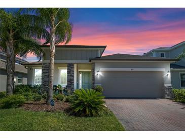Charming single-story home with a two-car garage, landscaped yard, and brick-paved driveway during a vibrant sunset at 861 Grazie Loop, Davenport, FL 33837