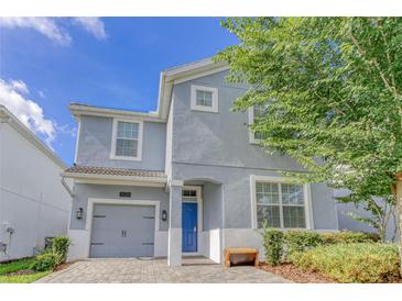 Charming two-story home with a blue door, a gray garage door, and landscaped front yard at 1628 Moon Valley Dr, Davenport, FL 33896