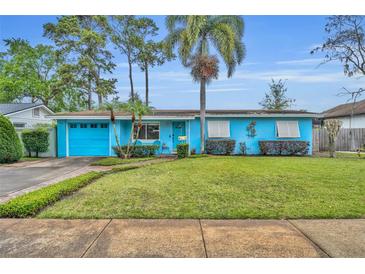Charming one-story blue home with a lush green lawn, garage, and vibrant landscaping at 2565 Brookshire Ave, Winter Park, FL 32792
