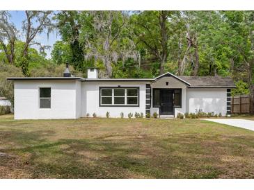 Charming single-story home with a white exterior and black trim nestled among mature trees on a well-manicured lawn at 239 S Lake Cortez Dr, Apopka, FL 32703