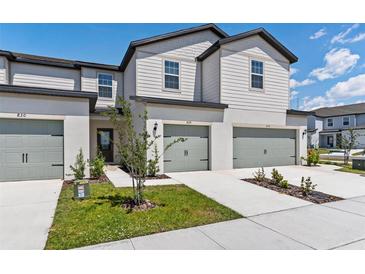 Townhome exterior with a gray garage door, landscaped yard, and white siding at 824 Poppy Ln, Dundee, FL 33838