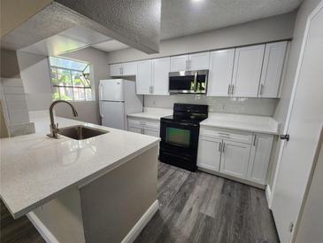 Bright kitchen featuring white cabinets, a stainless steel microwave, sleek countertops, and wood-look flooring at 200 Afton Sq # 108, Altamonte Springs, FL 32714