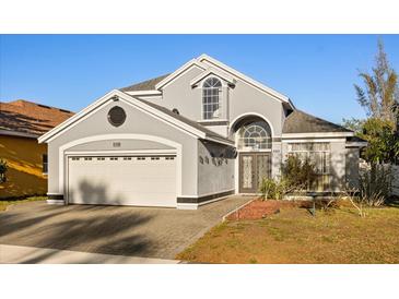 Home exterior with arched entryway, two-car garage, landscaped front yard, and gray paint at 12557 Crayford Ave, Orlando, FL 32837