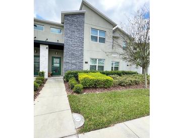 Modern townhome featuring manicured landscaping, a stone accent wall, and a welcoming green door at 428 Ocean Course Ave, Davenport, FL 33896