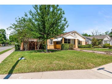 Beautifully landscaped front yard with mature trees and green lawn, with yellow home exterior and awnings at 335 W Bay St, Winter Garden, FL 34787