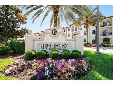 Attractive community sign nestled in lush landscaping including tropical palm trees and colorful flowers at 5550 E Michigan St # 2202, Orlando, FL 32822