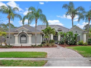 Charming single-story home featuring lush tropical landscaping, a brick driveway, and a stylish gray and white color scheme at 2218 Ridgewind Way, Windermere, FL 34786