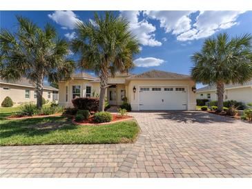 Charming single-story home with lush landscaping, a brick driveway, and a two-car garage at 5007 Belted Kingfisher Dr, Oxford, FL 34484