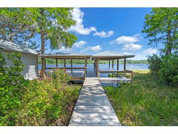 View of a wooden walkway leading to a charming covered dock with a beautiful lake view at 18618 Lake Pickett Rd, Orlando, FL 32820