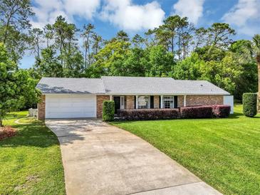 Charming brick home featuring a well-manicured lawn and a spacious driveway, surrounded by lush greenery and trees at 381 Red Mulberry Ct, Longwood, FL 32779