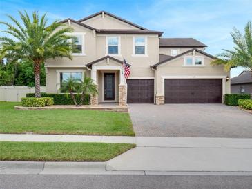 Inviting two-story home featuring a manicured lawn, palm trees, and a paver driveway leading to a two-car garage at 676 Bishop Bay Loop, Apopka, FL 32712