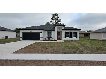 Charming single-story home featuring a dark garage door, orange front door, and freshly installed landscaping at 699 Marion Oaks Trl, Ocala, FL 34473