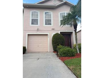 Two-story pink townhouse features a one car garage, simple landscaping, and a dark brown front door at 2737 Merrieweather Ln, Kissimmee, FL 34743