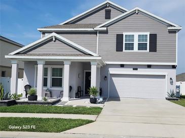 Charming two-story home featuring gray siding, a covered porch with white columns, and an attached two-car garage at 1803 Perch Hammock Loop, Groveland, FL 34736
