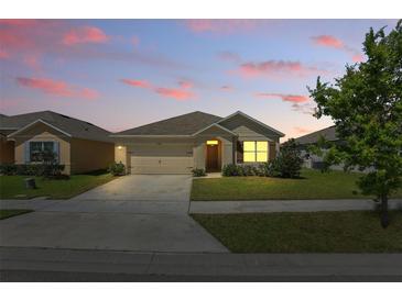 Charming one-story home with a well-manicured lawn, two car garage, and inviting front entrance at dusk at 3348 Perennial Ln, Kissimmee, FL 34746