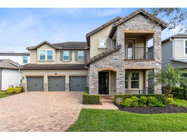 Charming two-story home featuring stone accents, a balcony, a three-car garage, and a well-manicured lawn at 1675 Amsel Falls Park Ter, Winter Garden, FL 34787