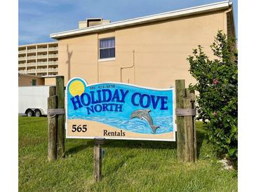 Holiday Cove North rental sign with dolphin against a tan building with nice grass at 573 N Atlantic Ave # 5, New Smyrna Beach, FL 32169