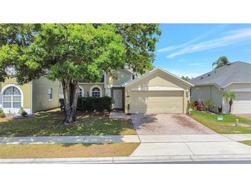 Charming home featuring a well-manicured lawn, brick driveway, attached two-car garage, and mature tree at 9999 Shadow Creek Dr, Orlando, FL 32832