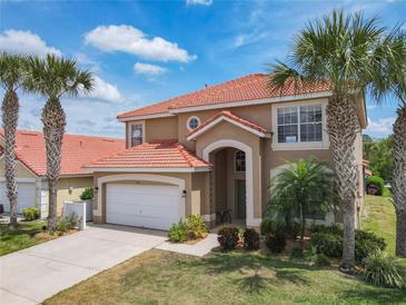 Stunning two-story home featuring a red tile roof and lush landscaping with palm trees, creating a tropical paradise at 330 Rosso Dr, Davenport, FL 33837