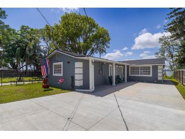 Charming gray home featuring a spacious driveway, well-kept lawn, and patriotic American flag waving in the breeze at 30 Sunset Cir, Lake Alfred, FL 33850