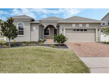 Beautiful home featuring a manicured lawn, landscaped garden beds, and a brick paver driveway at 16936 Champlain St, Clermont, FL 34714