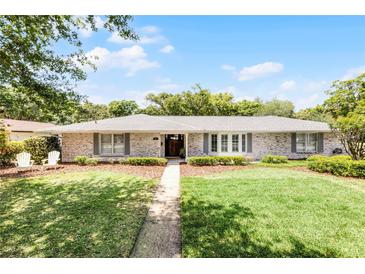 Charming brick home featuring a manicured lawn, walkway, and two white Adirondack chairs on a beautiful sunny day at 901 Golfside Dr, Winter Park, FL 32792