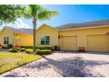 Charming yellow single-Gathering home with a two-car garage, lush landscaping, and a brick driveway on a sunny day at 3205 Sonesta Ct # F, Clermont, FL 34711