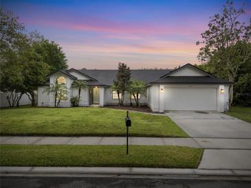 Charming single-story home with well-manicured lawn, lush trees, and a beautiful twilight sky at 1012 Willa Lake Cir, Oviedo, FL 32765