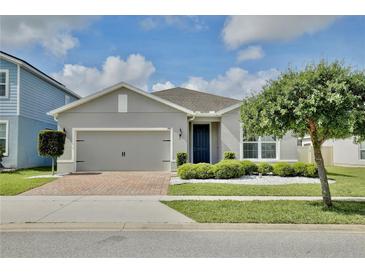 Charming single-story home with a brick driveway, manicured landscaping, and a gray stucco exterior at 299 Whirlaway Dr, Davenport, FL 33837