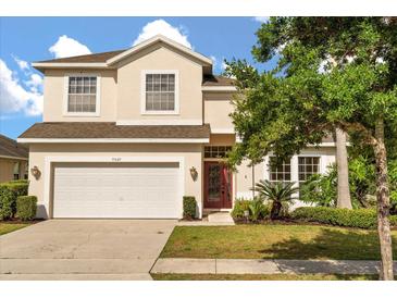 Two story home with a two car garage, manicured lawn and garden, and a red front door at 9469 Edenshire Cir, Orlando, FL 32836