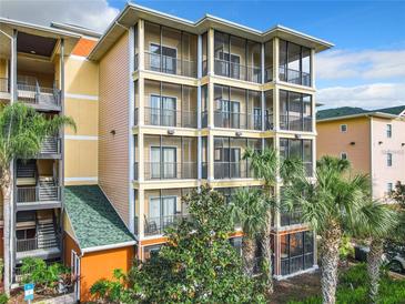 Condo exterior featuring screened balconies, tropical landscaping, and colorful architectural design at 9051 Treasure Trove Ln # 405, Kissimmee, FL 34747