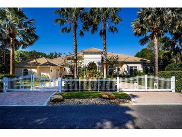 Stunning estate with white fence and brick driveway, showcased with palm trees against a clear, sunny sky at 4 Island Dr, Lake Mary, FL 32746