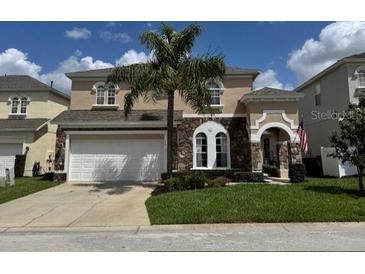 Two-story home with stone accents, arched windows, a palm tree, and a well-manicured lawn at 462 Tupelo Cir, Davenport, FL 33897