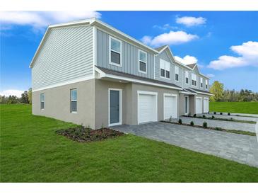 View of townhomes with one car garages, blue siding, paved driveways, and green lawns on a sunny day at 1419 Fan Palm Dr, Davenport, FL 33897